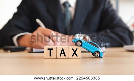 Concept of tax of car. Words TAX on a woodblock with toy car and man signing purchase documents in background, manage for success business.
