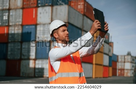 Taking photos by using tablet. Male worker is on the location with containers.