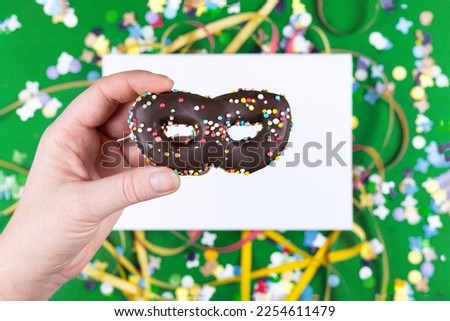 Female hand holding chocolate chip cookies in the form of a carnival mask, flat lay 