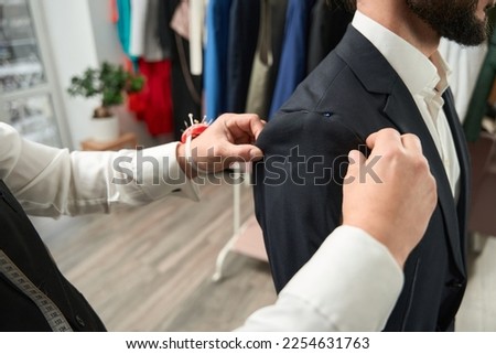 Experienced clothier altering suit jacket of client Royalty-Free Stock Photo #2254631763
