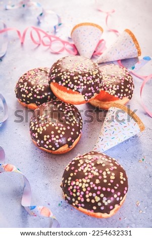 Chocolate Berliner pastry for carnival and party. German Krapfen or donuts with streamers and confetti.  Colorful carnival or birthday image