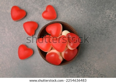 Bowl and delicious heart shaped jelly candies on grey table, flat lay