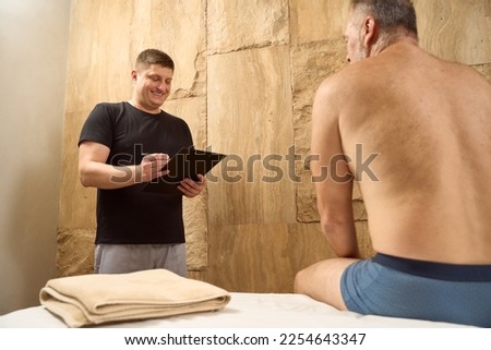 Elderly man sits on a massage table with bare torso Royalty-Free Stock Photo #2254643347