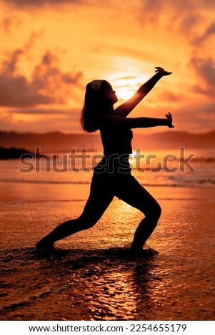 the silhouette of an asian teenager in black clothes posing with her body above the seaside waves very beautifully in the morning