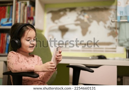 Little girl wear headphones watching cartoons or kid video on her phone. 