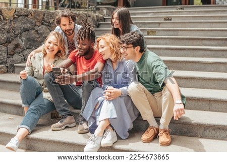 group of diverse z generation people sitting on staircase playing with cell phone