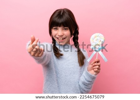 Little caucasian girl holding a lollipop making money gesture