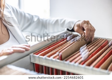 The clerk is leafing through stored folders, looking for a file or document. Concept of data storage, filing cabinet and business administration. Royalty-Free Stock Photo #2254682601