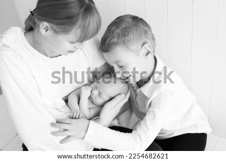 newborn baby in the arms of mother and older child, black and white photo, monochrome. parental care for a new life