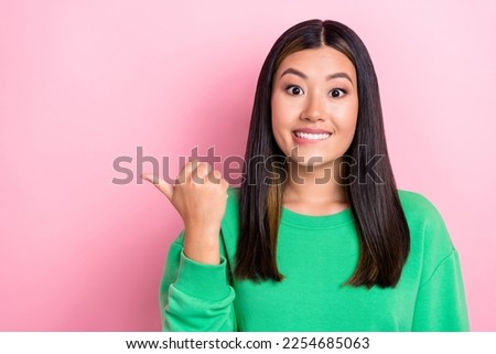 Photo of young positive mood smile cheerful japanese lady wear jumper bite lip excited wish finger point mockup isolated on pink color background