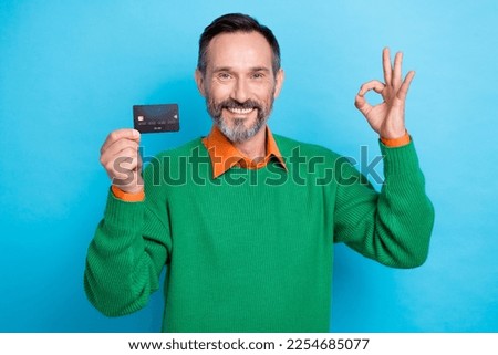 Photo of positive good mood smile professional banker wear green jumper show okey sign hold plastic card promo isolated on blue color background