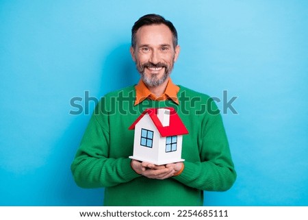 Photo portrait of mature attractive male holding little house mortgage rate wear trendy green outfit isolated on blue color background