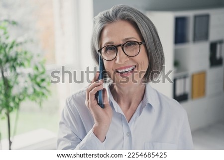 Photo of beautiful positive aged lady banker speak communicate telephone coworking workplace indoors