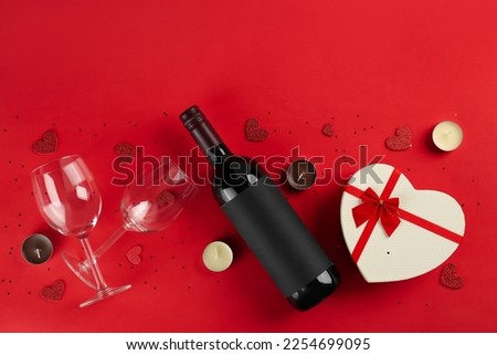 Bottle of wine, glasses, gift and hearts on red background. Valentine's Day Celebration