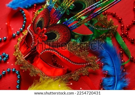 Carnival masks for Mardi Gras celebration with feathers and beads on red background, closeup