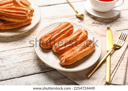 Plates with tasty eclairs on light wooden background Royalty-Free Stock Photo #2254724449