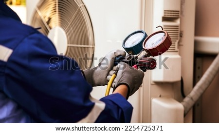 Heat and Air Conditioning, HVAC system service technician using measuring manifold gauge checking refrigerant and filling industrial air conditioner after duct cleaning maintenance outdoor compressor. Royalty-Free Stock Photo #2254725371