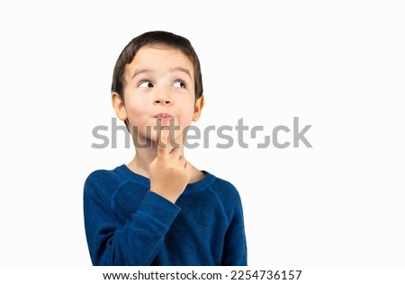 Pensive kid looks away at copy space thinking isolated on a white background, funny kid lips hold finger near mouth conceiving some kind of joke, conceptual image Royalty-Free Stock Photo #2254736157