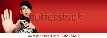 elegant nonbinary person in black beret showing stop gesture isolated on red, banner