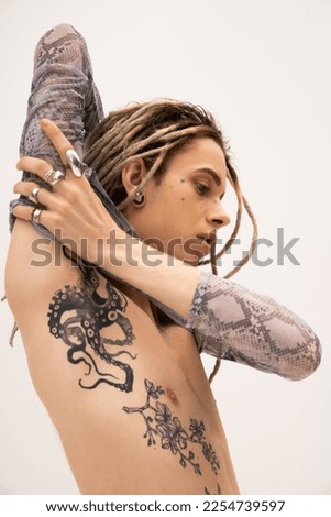 Tattooed queer person in crop top with animal print touching arm isolated on white