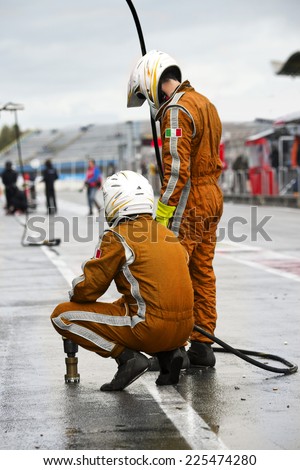 Pit Crew anticipating the arrival of their race car during a tyre change pitstop because of wet race conditions Royalty-Free Stock Photo #225474280
