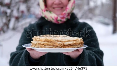 Close-up. A woman holds a plate of pancakes outdoors in winter. Traditional thin Russian pancakes on a plate. Baking for Shrove Tuesday in Russia. Royalty-Free Stock Photo #2254746393