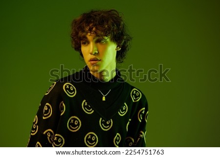 Man fashion and style accessories model with curly hair stylish sweater, hipster teen lifestyle, close-up portrait on green background mixed neon light, copy space