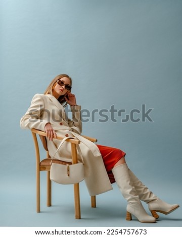 Fashionable confident woman wearing elegant white woolen coat, sunglasses, high leather heeled boots, posing on blue background. Full-length studio fashion portrait. Copy, empty space for text Royalty-Free Stock Photo #2254757673