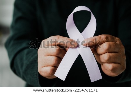 Women's hands holding a pink or purple ribbon bow as a symbol of the fight against breast cancer (other types of cancer). World Cancer Awareness Month and World Cancer Day concept.