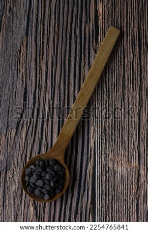 Pile of melt chocolate buttons, placed on a wooden spoon, on a wooden background. Ready to be melted, or stirred into cookie dough. Picture taken above the spoon.