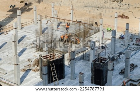 The construction of a monolithic-frame building, a team of builders sets in place a section of metal reinforcement filed by a crane. Slinger at work. Formwork elements. Royalty-Free Stock Photo #2254787791