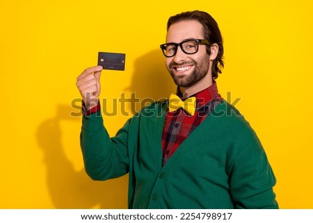 Photo of young toothy smiling guy wear stylish green cardigan hold black plastic credit card promotion investment isolated on yellow color background