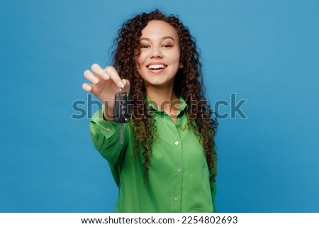 Young cheerful fun happy woman of African American ethnicity 20s she wear green shirt hold give car keys fob keyless system isolated on plain blue background studio portrait. People lifestyle concept