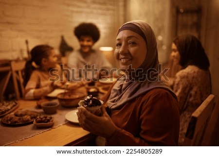 Happy Muslim mature woman date fruit while having dinner with her extended family and looking at camera.  Royalty-Free Stock Photo #2254805289