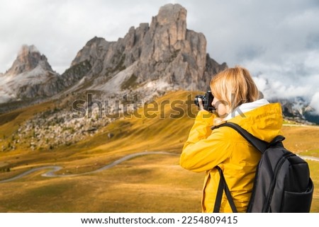 Professional photographer takes pictures of Passo Giau pass using camera. Woman with backpack enjoys activity in Italian Alps 