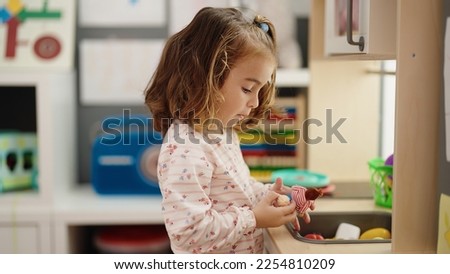 Adorable hispanic girl playing with doll and play kitchen at kindergarten