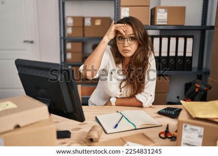 Young hispanic woman working at small business ecommerce worried and stressed about a problem with hand on forehead, nervous and anxious for crisis 
