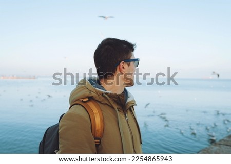Young cheerful man walking by the sea in winter time. Travel and active lifestyle concept