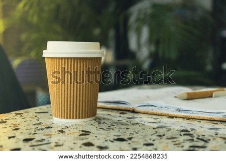 Hot latte coffee in craft recycling paper cup with paper notebook. Coffee break. Online job or studying co-working space A take away paper cup on cafe table. Freelance Workspace notebook with coffee