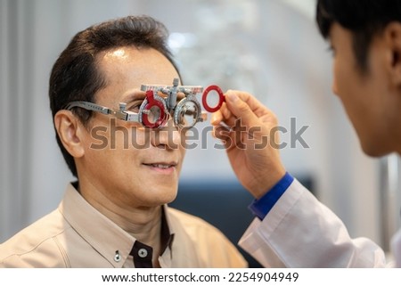 Portrait of young ophthalmologist putting trial frame on male patient during vision check in modern clinic Royalty-Free Stock Photo #2254904949