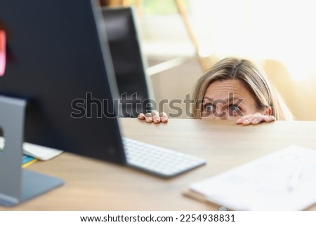 Scared female manager hidden behind office desk and looking at computer screen. Unwanted communication, mistake in work and shyness concept. Royalty-Free Stock Photo #2254938831