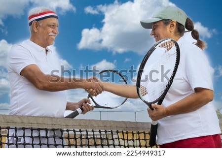 Older couple shaking hands on tennis court.