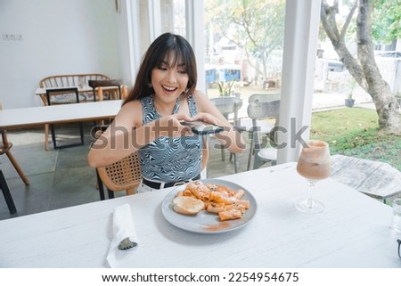 Smiling casual woman taking a picture of pasta on a white plate with mobile phone while sitting at the restaurant
