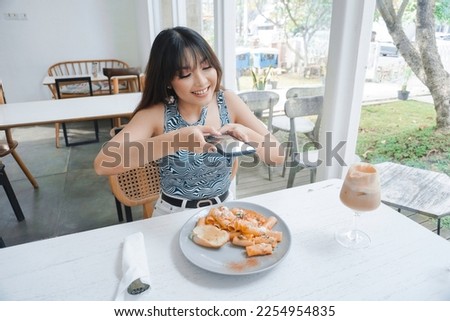 Smiling casual woman taking a picture of pasta on a white plate with mobile phone while sitting at the restaurant