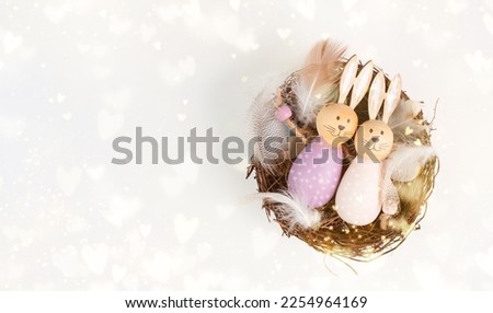 Easter bunny or rabbit couple cuddle together in a wicker nest with bird feathers and hearts, spring holiday greeting card
