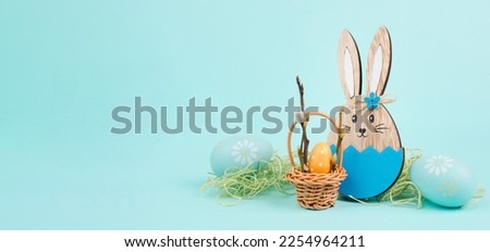 Easter bunny or rabbit sitting next to a wicker basket filled with colorful eggs, spring holiday 