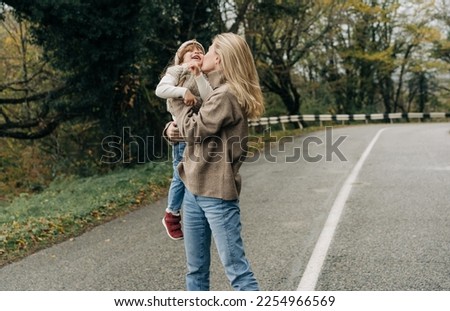 A cheerful young mother is spinning in embracing with her little daughter on a walk.