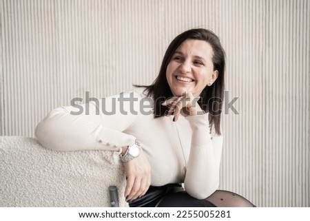 The boss is a business woman smiling, showing her teeth, in beige office clothes. Good mood in the office during the day.