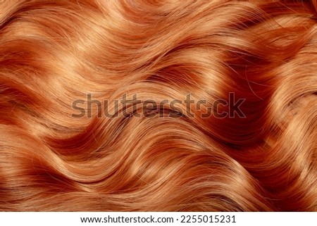 Red hair close-up as a background. Women's long orange hair. Beautifully styled wavy shiny curls. Hair coloring bright shades. Hairdressing procedures, extension. Royalty-Free Stock Photo #2255015231