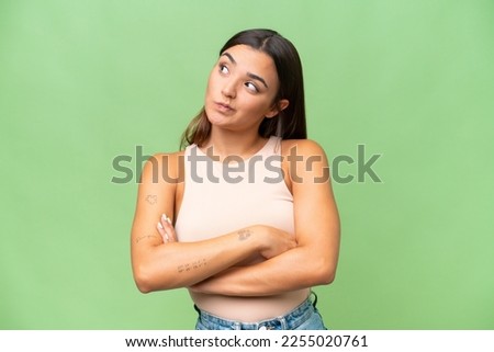 Young caucasian woman isolated on green chroma background making doubts gesture while lifting the shoulders
